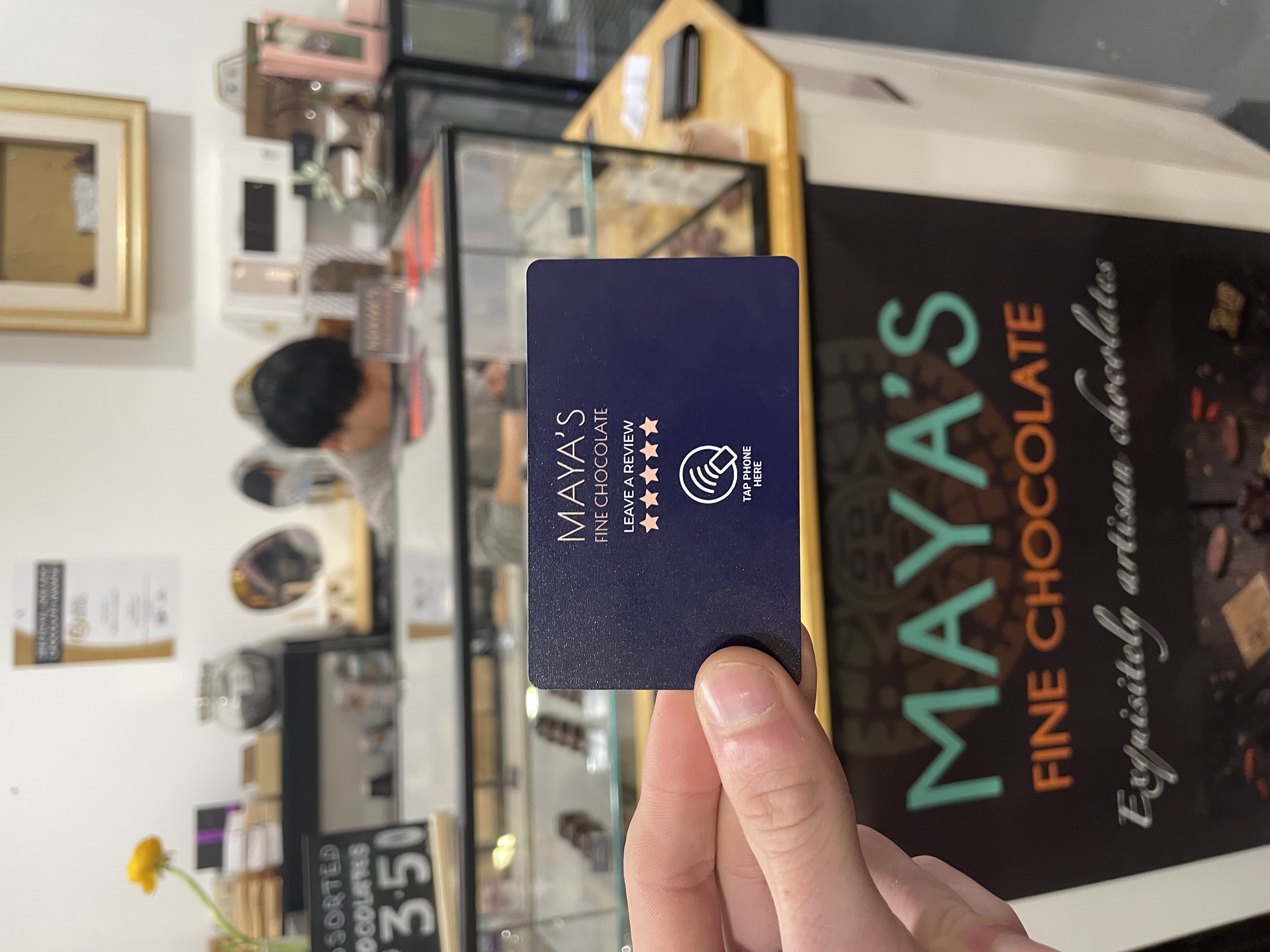 Maya's Fine Chocolate TapReview card being held in their store